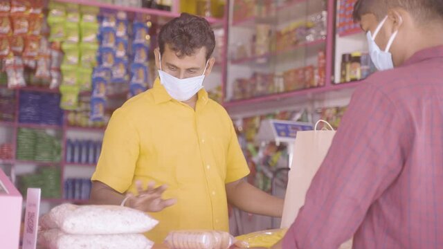 grocery Merchant packing groceries for customer by receiving money while both in medical face mak during coronavirus or covid-19 pandemic - concept of small local business reopen with safety measures