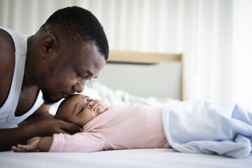 Black father kissing forehead of newborn daughter