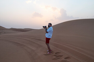 Man is a professional photographer with a camera in the desert among the Arabian sand dunes, Dubai United Arab Emirates