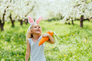 Cute funny girl with Easter eggs and bunny ears at garden. easter concept. Laughing child at Easter egg hunt. Child in park with basket full of eggs, spring concept