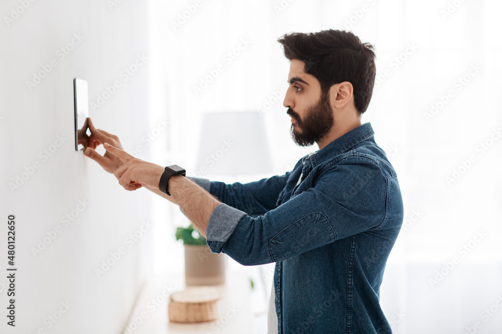 Poster Automation domestic system. Arab man using digital tablet on wall with smart home control system app, side view