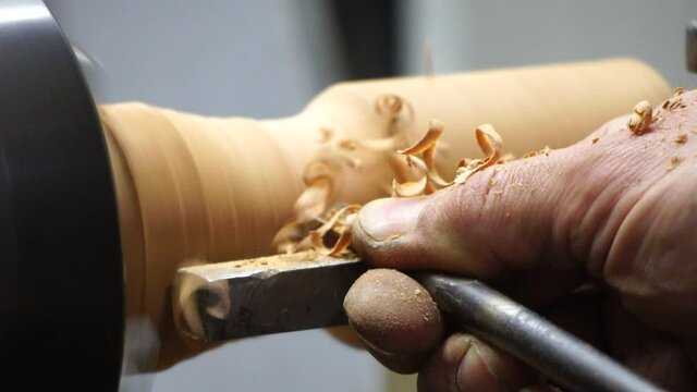 Man carpenter using chisel for shaping piece of wood on turning lathe machine with many shavings at workshop - close up. Slow motion. Carpentry, hobby, craftsmanship and woodworking