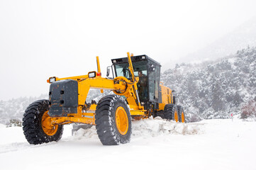 The bulldozer or grader cleans snow on the road