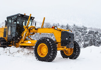 The bulldozer or grader cleans snow on the road