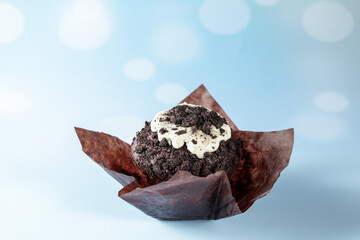 Chocolate muffin with white cream and crumbs in open brown paper form on light blue background. Happy birthday or pastry shop card with copy space