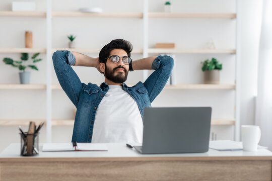 Successful arab freelancer guy resting holding hands behind head, relaxing at workplace after online work