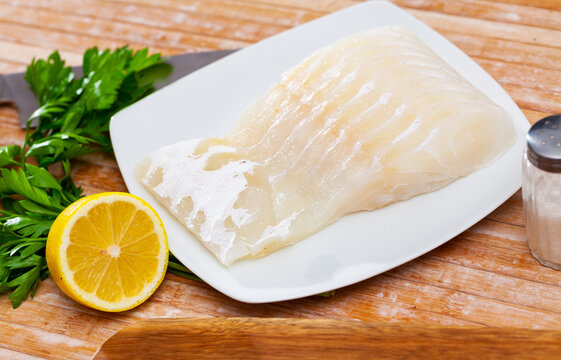Raw fish with condiments, kingklip fillet with parsley and lemon on wooden table