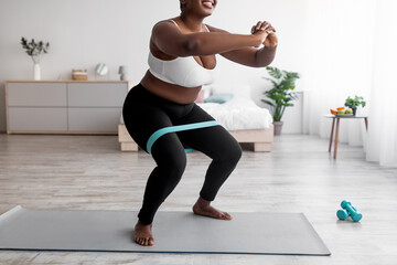 Cropped view of curvy black woman squatting with rubber band on domestic workout