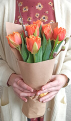 Florist hands holding a bouquet of fresh orange tulips, wrapped in kraft paper. Women Day gift.