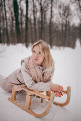 a beautiful young girl rides a sleigh in the winter forest, winter entertainment, a girl runs with a sleigh in the park