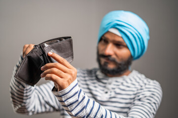 Worried young sikh man for not having money in wallet - concept of debt, bankrupt and unemployment.