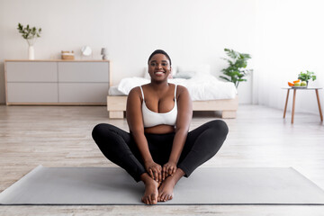 Cheerful plus size black woman doing yoga on sports mat at home, free space