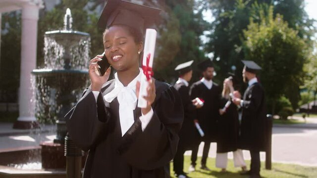 Great looking black woman student graduate she discussing excited with someone on the phone very excited explain something in front of the camera in the college garden