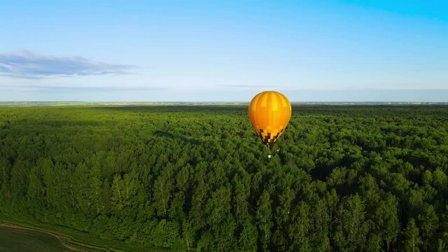 A yellow nylon balloon flies over the forest. A propane burner shoots out a flame, heating the air in the envelope. Wild endless forest from bird's eye view at sunset. Concept of adventure and freedom