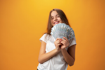 Happy teenage girl holding lots of money against yellow background