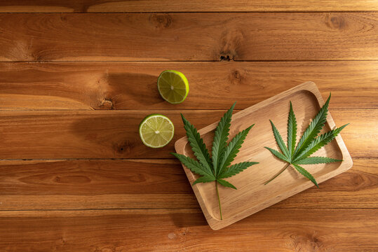 Photo of cannabis leaves in a wooden tray with lemon on a wooden table with warm light and shadow background. Copy space Decoration for backdrop artwork design or Banner. Eatable vegetable concept