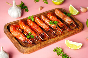 Cooked shrimp and langoustines, king prawns with lime, garlic and parsley. Grilled and fried on pink background