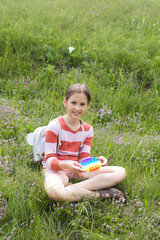 A little cute girl is sitting on the grass with a pop it - antistress toy.
