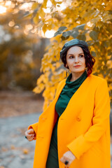 Beautiful woman walks outdoors in autumn. She is wearing a yellow coat and a green dress. Young woman enjoying the autumn weather. Autumn content.