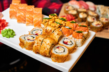 Waiter holding a set of sushi rolls on a white plate. Close-up, selective focus.