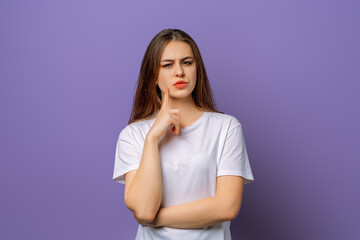 Portrait of thinking looking beautiful young brunette in white t shirt, standing over purple background