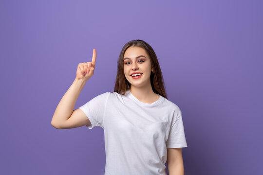 Pretty young woman with long hair pointing finger up, raising eyebrows up surprised, showing advertisement, standing over purple background