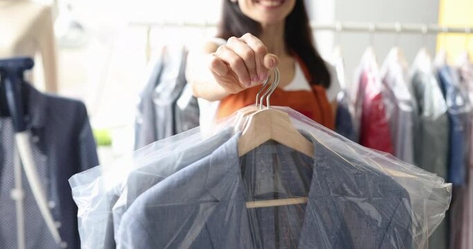 Smiling receptionist at dry cleaning hands over clothes to client