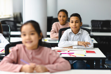 Portrait of small boy sitting at desk in classroom