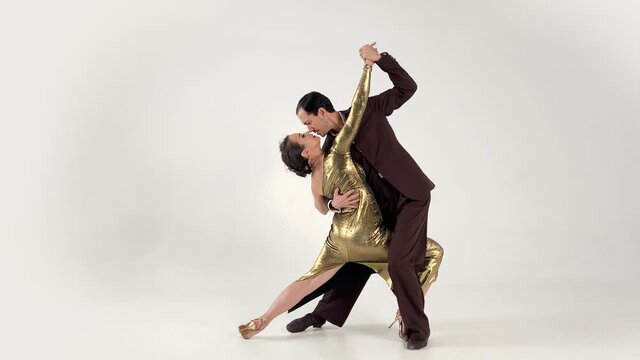 Spectacular ending of the tango dance performed by a couple of professional dancers in elegant suit and gold dress with the leg thrown high.