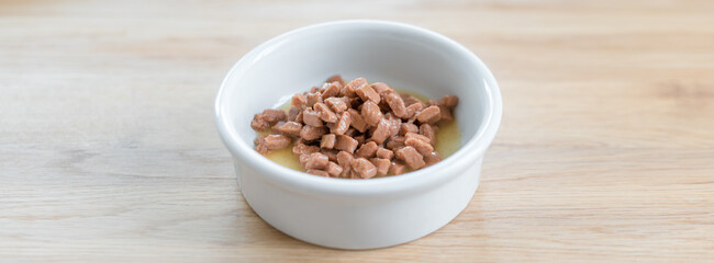 Wet food for cats and dogs in a white bowl on wooden floor close up