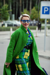 Portrait of fashionable adult woman wearing colorful bright accessories, sunglasses, green stylish coat. Bright fashion model with short hair, street style