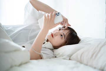 ベッドの上でスマートフォンを操作する女性