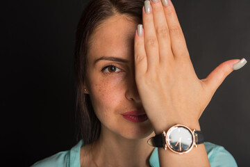 portrait of a young pretty girl covering half face with her hand and looking straight at dark...