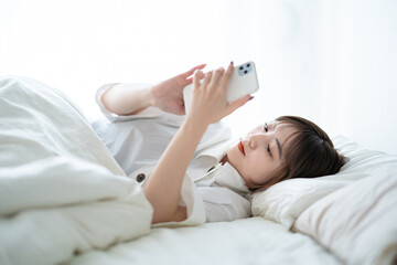 ベッドの上でスマートフォンを操作する女性