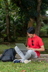 Young student on the grass in the park sits under a tree and  works with a laptop.