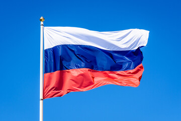 Fototapeta na wymiar The national flag of Russia is flying in the wind at full mast against blue sky.