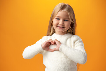 Happy little girl showing heart love gesture over yellow background