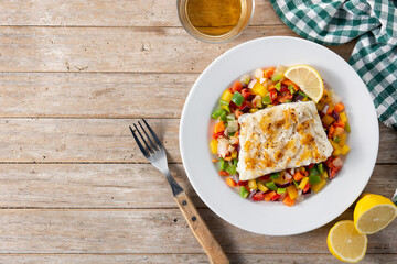 Grilled cod with vegetables in plate on wooden table. Top view. Copy space