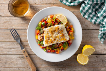 Grilled cod with vegetables in plate on wooden table