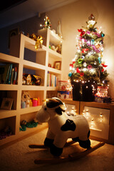 Hobby cow toy against Christmas tree with shining garlands on evening home.