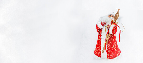 A toy Santa Claus in a snowy forest in the snow. Place for text, copy space