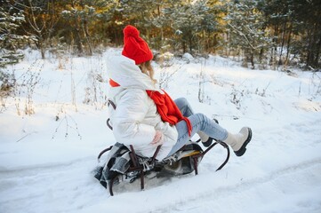Beautiful young woman wearing a warm winter clothes, sitting on a sleigh and sliding down the hill, having fun on a snowy winter day