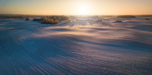Winter aerial panorama with wavy meadows covered in snow, early morning light