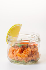 Raw salmon tartare in a glass jar with a slice of lime. On a white background. Isolate
