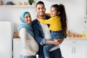 Portrait Of Smiling Muslim Family With Pregnant Mother And Little Female Kid In Kitchen