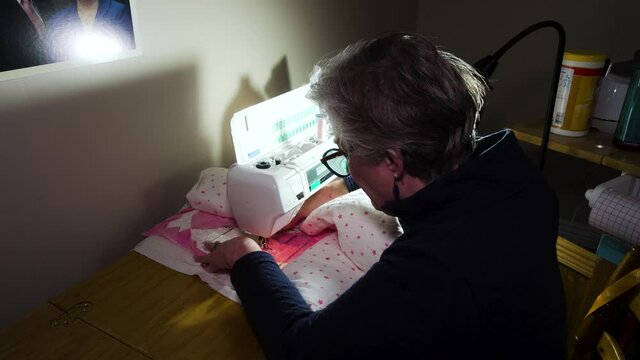 Mature woman sewing a heart pattern on a homemade quilt with a template on her sewing machine