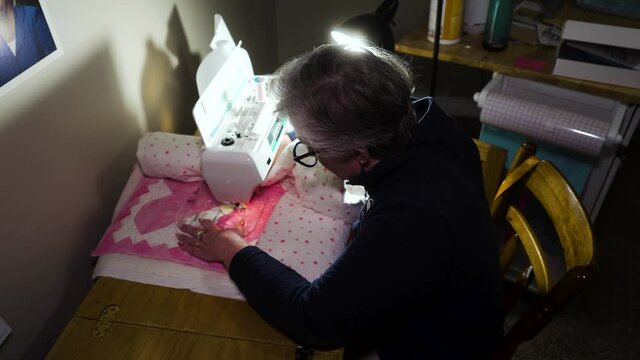 Senior woman machine sewing a pattern on a homemade quilt in her craft room