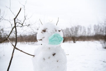 a snowman in a medical mask stands in the middle of a snow garden