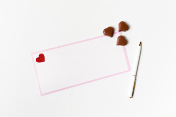 Romantic letter, white blank greeting card with a pen and heart-shaped chocolate candies on white