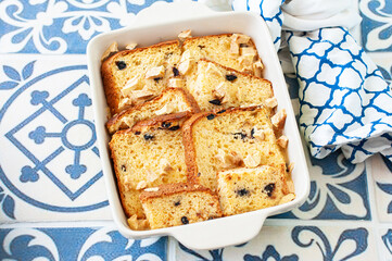 Bread (panettone) pudding from leftovers with custard and raisins in a baking dish on a blue background. - 480146264